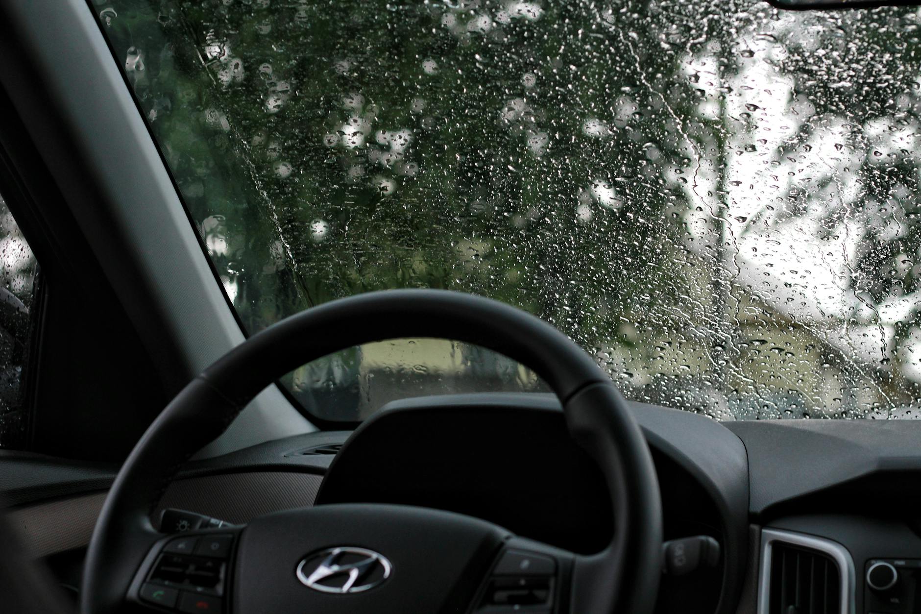 Widok z wnętrza auta przez zalaną deszczem przednią szybę