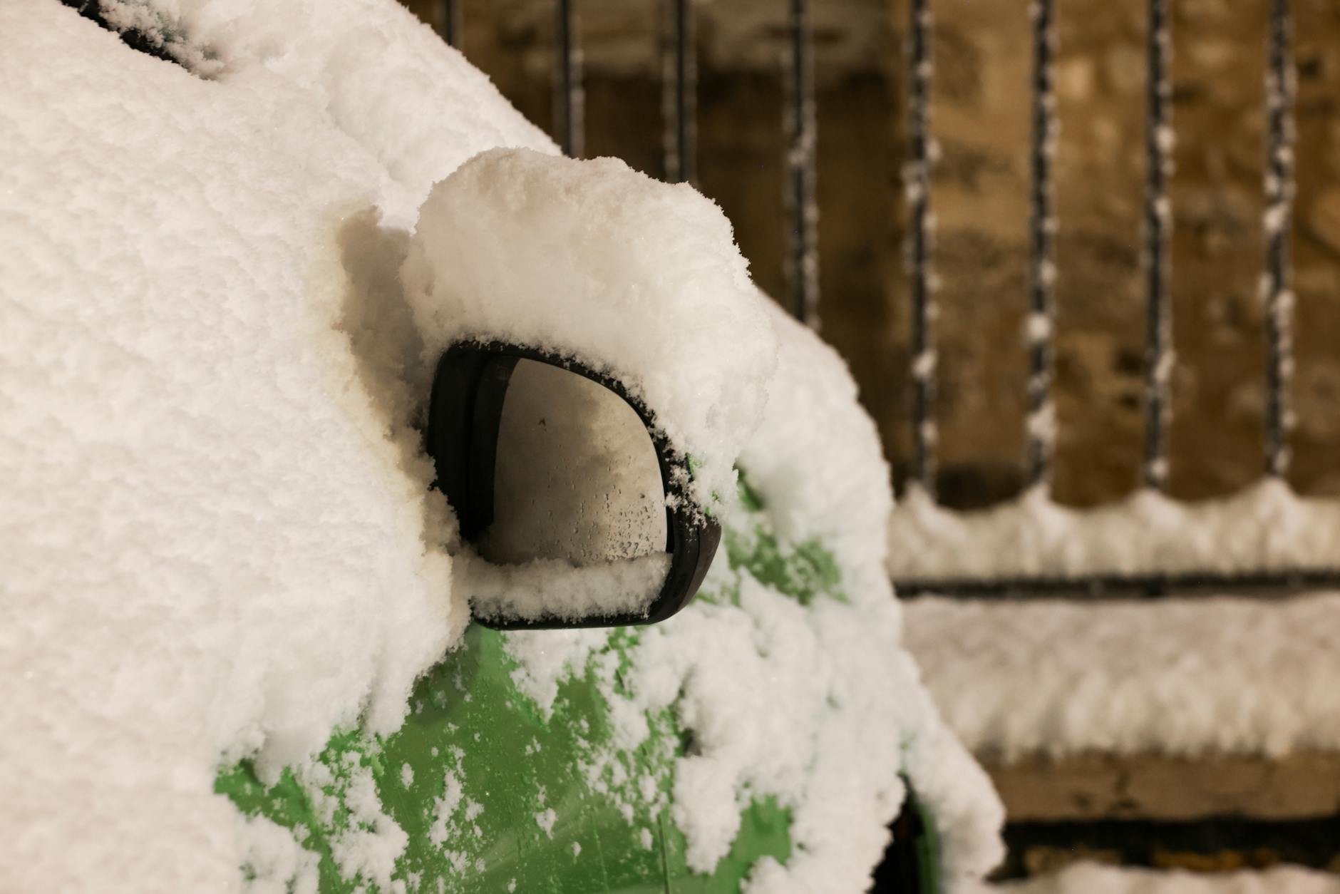 Zaśnieżone lusterko zielonego auta zimą z bliska